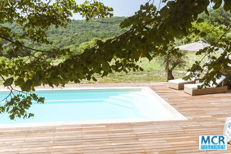 Installation d'une Piscine Coque modèle MATAURA à  SAINT-FÉLIX-DE-PALLIÈRES à coté d'Alès, avec volet immergé de couleur beige et margelles en travertin beige.