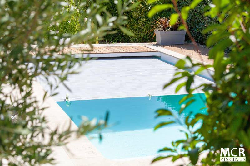 MOTU : Piscine coque polyester avec volet immergé, un escalier d'angle et une plage