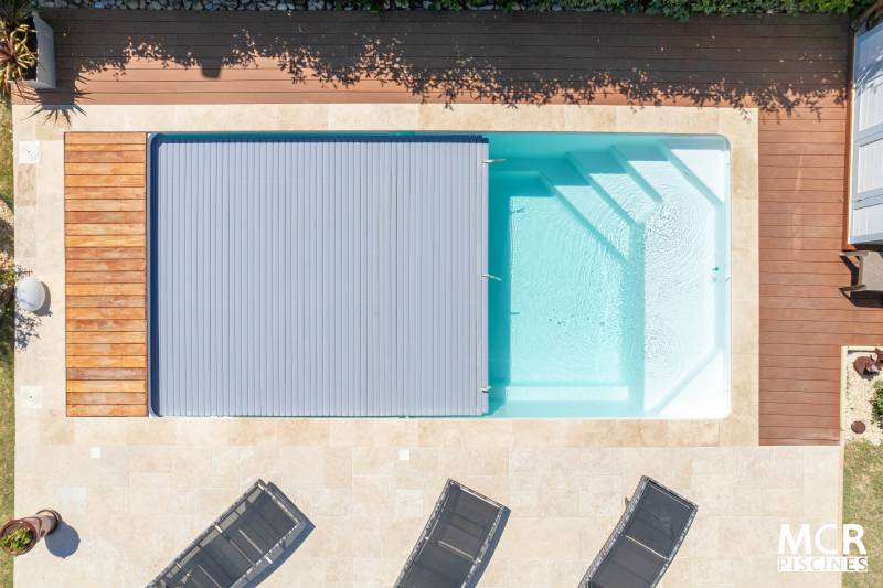 MOTU : Piscine coque polyester avec volet immergé, un escalier d'angle et une plage